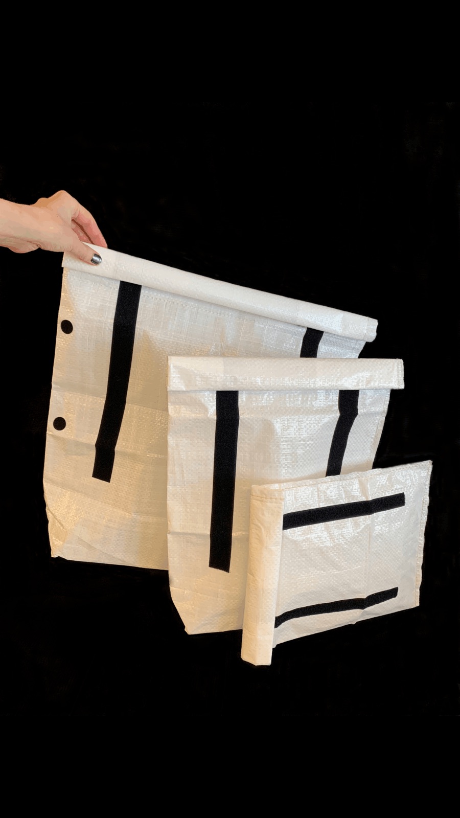 Drei weiße Ravioli Taschen stehen vor dunklem Hintergrund nebeneinander. Eine Hand greift nach der hintersten Tasche.